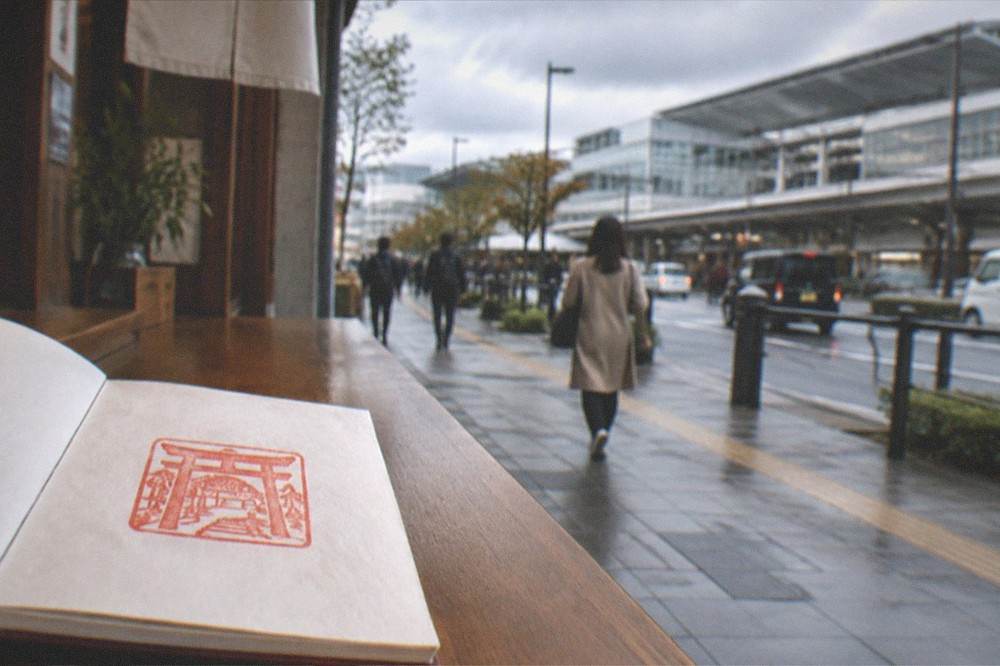 A hand-inked red shrine seal stamp in a folded book on a wooden counter