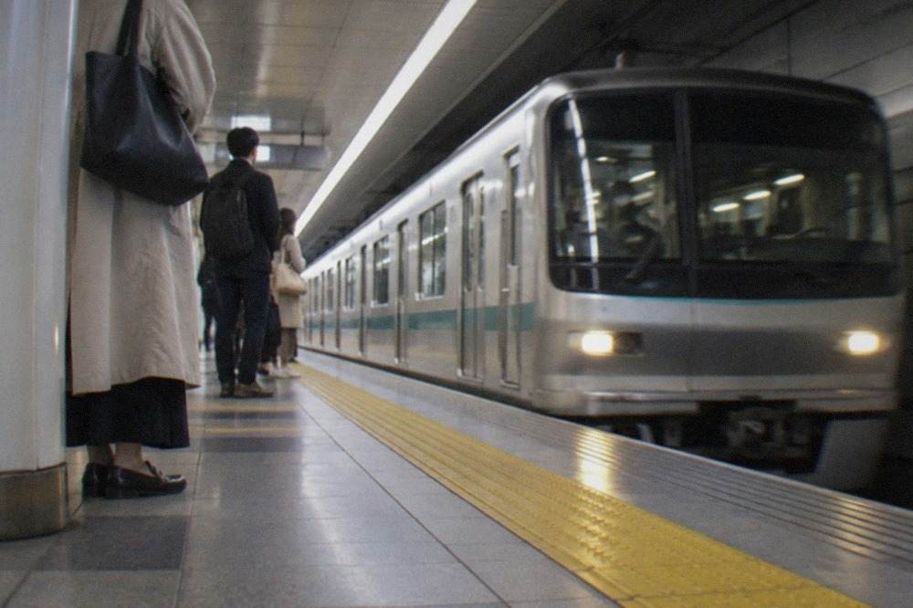 A Kyoto subway platform with a train arriving and passengers waiting behind the yellow safety line