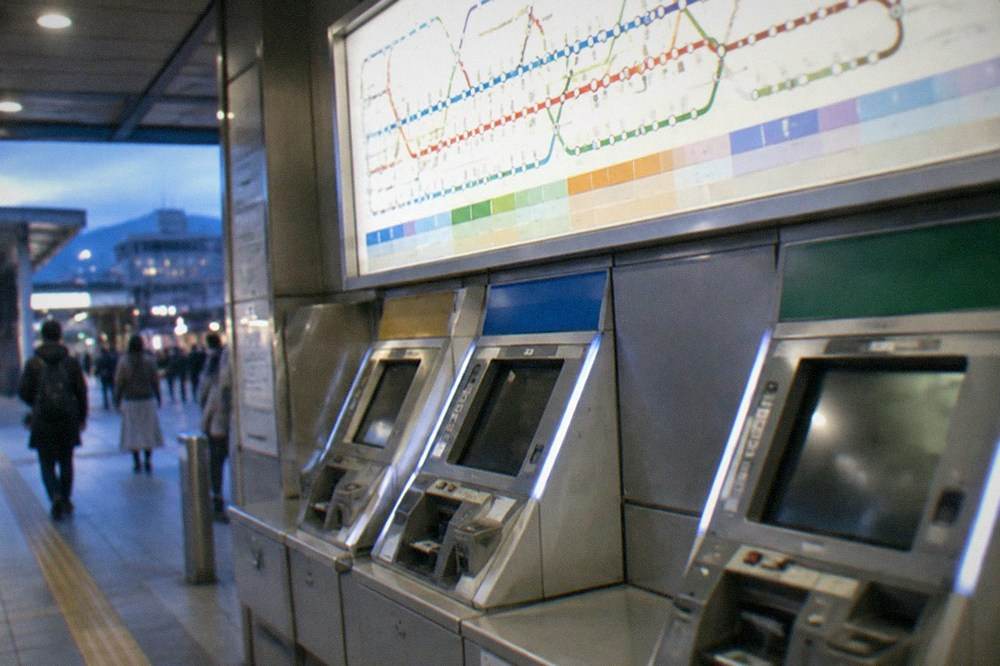 A row of Kyoto subway ticket machines with a bilingual fare chart above them