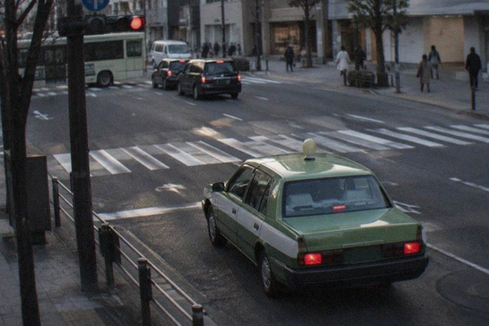 A green and white Kyoto taxi waiting at a signalised downtown intersection in the evening