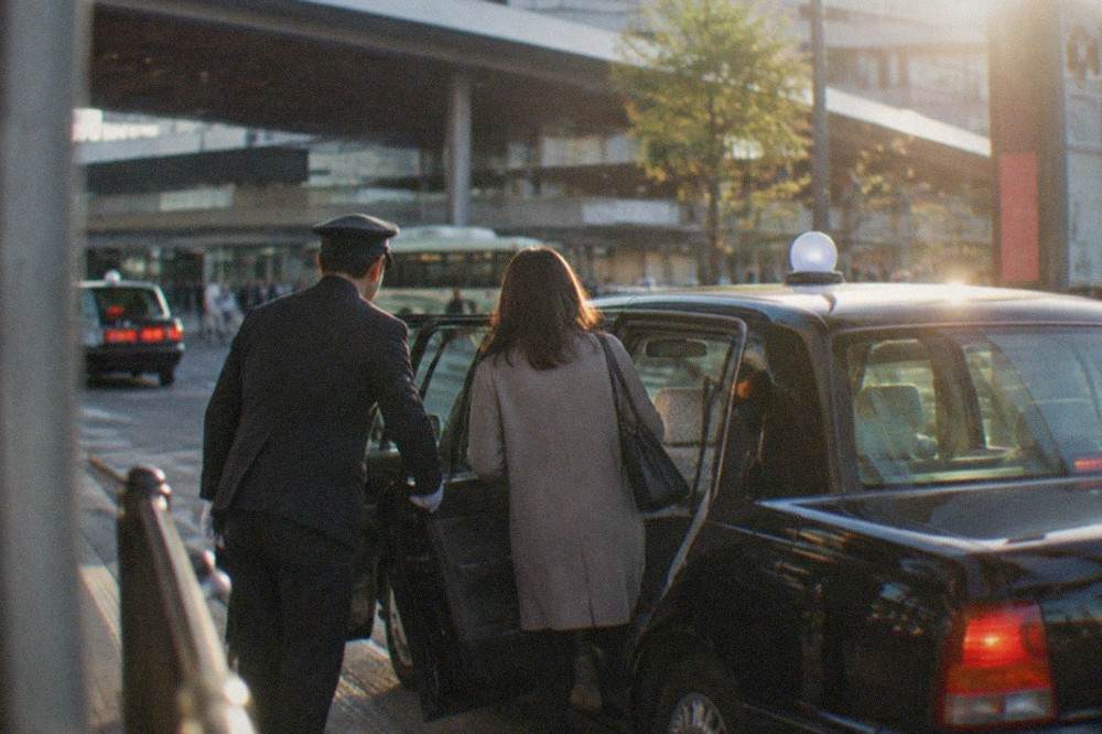 A passenger stepping into a taxi with its door opened automatically by the driver outside Kyoto Station