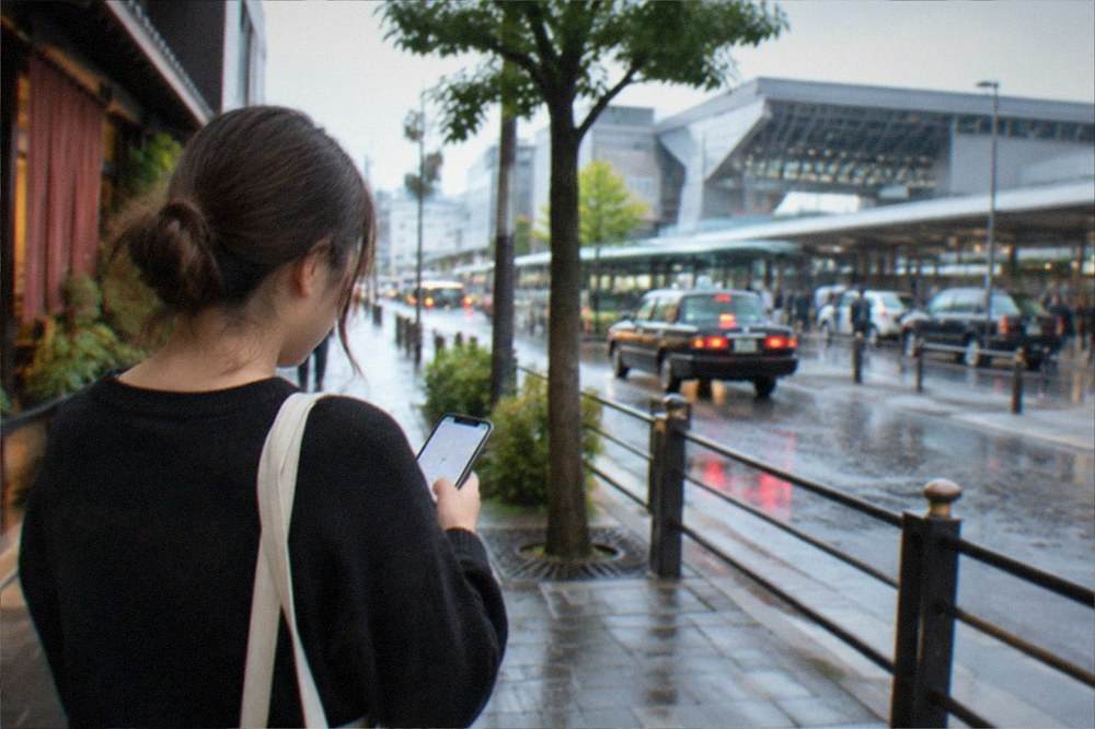A visitor checking a ride-hailing app on a smartphone while standing on a Kyoto sidewalk