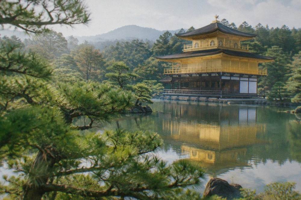 Golden pavilion of Kinkaku-ji reflected in the pond beside it, with pine trees in the foreground
