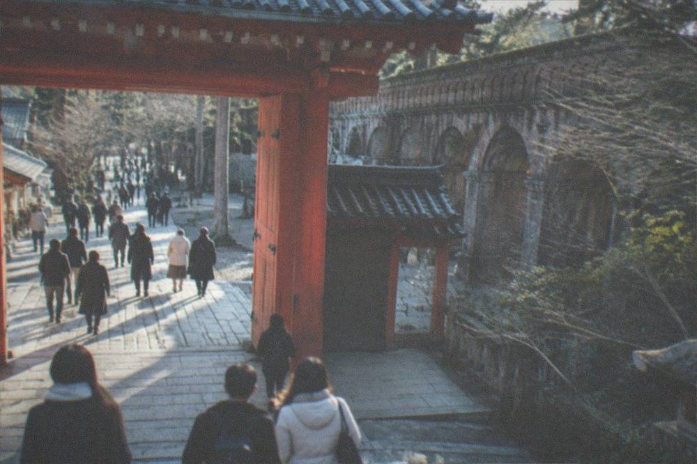 Visitors walking through the temple gate and stone path at Nanzen-ji with the brick aqueduct behind