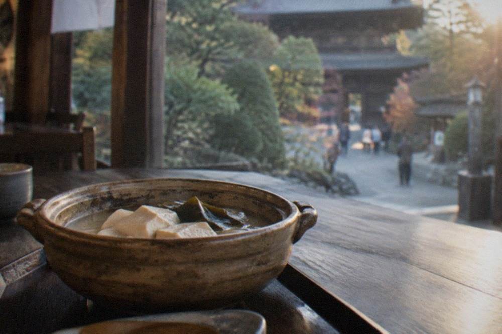 A clay pot of simmered tofu with kombu on a dark wooden table in a Kyoto restaurant