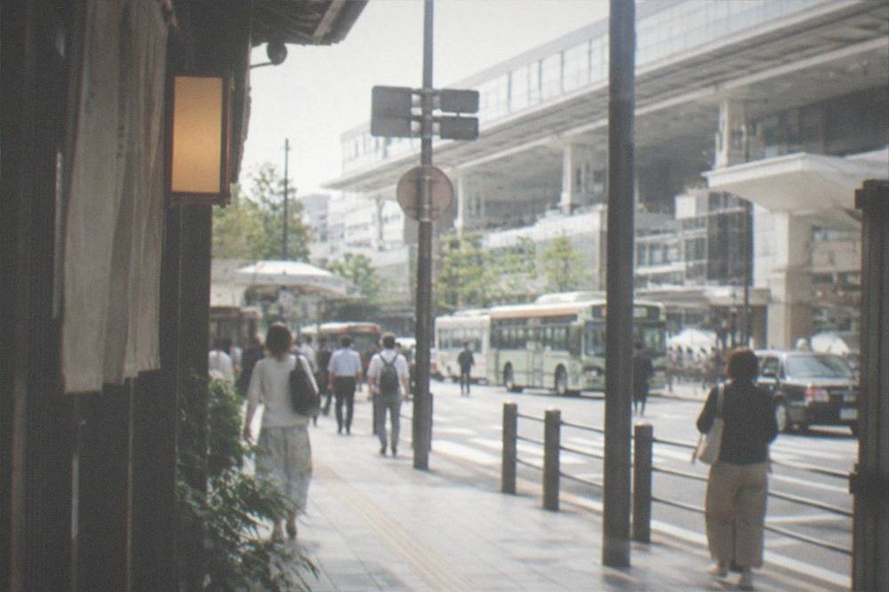 A green Kyoto city bus stopped at a busy street corner with passengers boarding