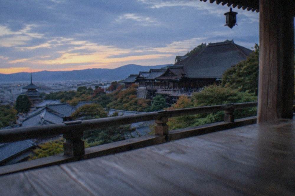 Kyoto temple rooftops and forested hills seen from a wooden temple veranda at golden hour