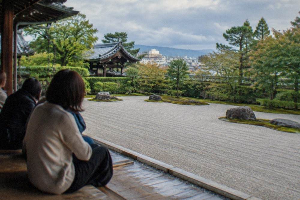 Visitors seated on a long wooden temple veranda looking out over a rectangular raked gravel garden