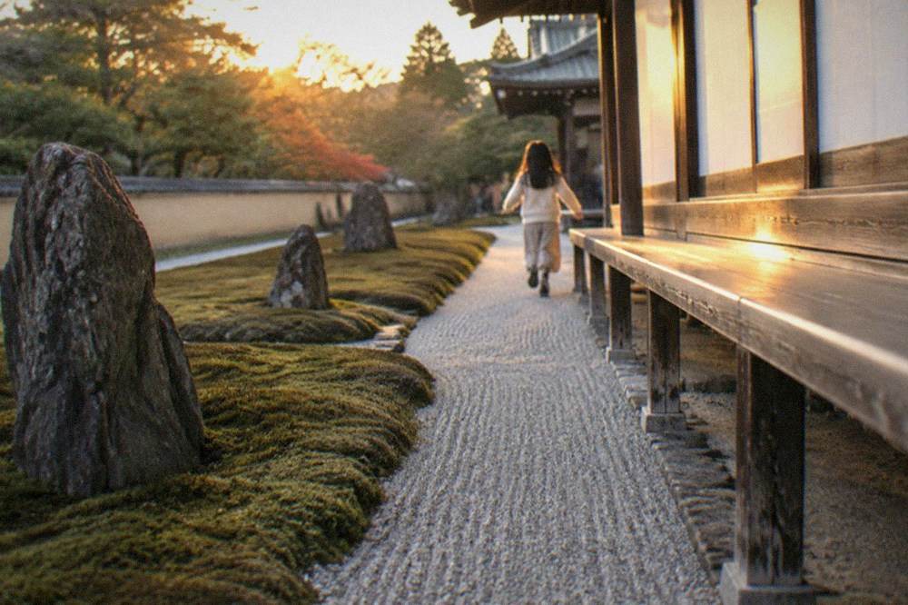 A narrow strip of raked white gravel flowing between moss and upright stones along a temple building's edge