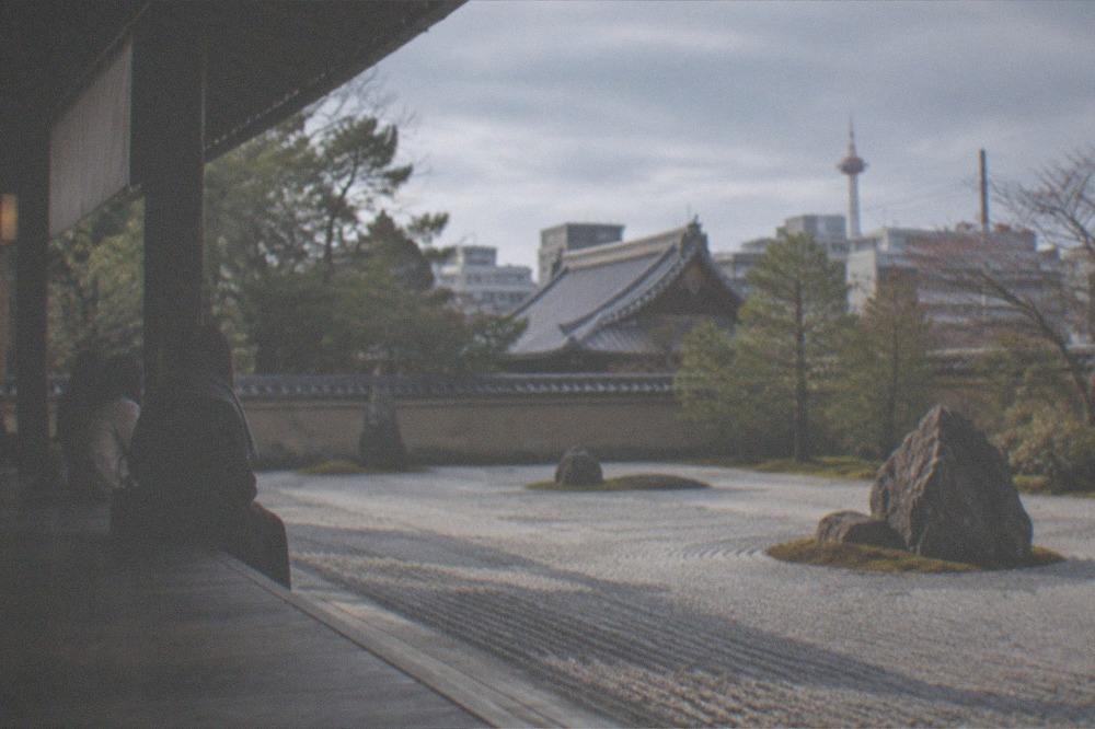 A zen garden at dawn with long shadows across raked gravel and a few seated visitors on the veranda