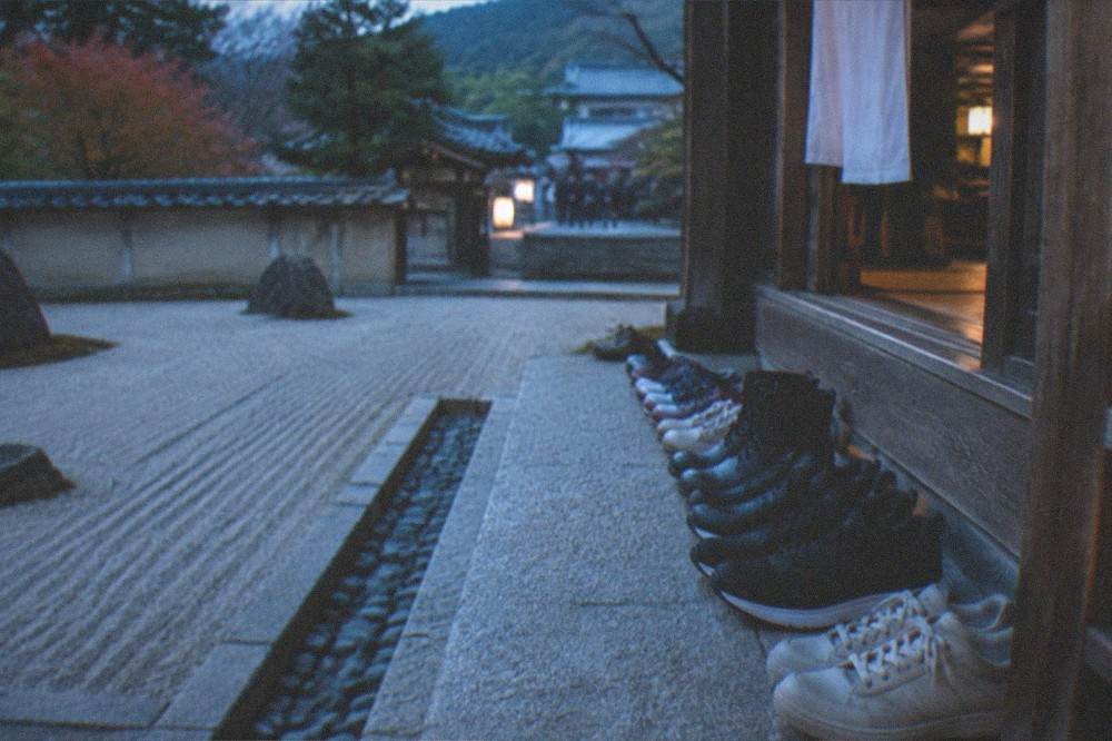 A row of visitors' shoes neatly lined up on a stone step beside a wooden temple entrance
