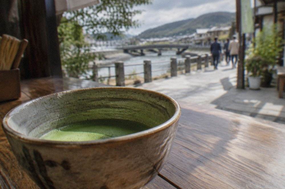 A bowl of bright green matcha whisked in a ceramic tea bowl on a wooden counter