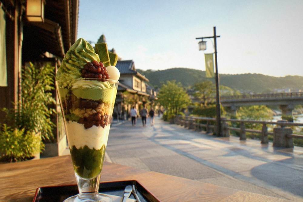A tall matcha parfait with layered cream, red bean and jelly in a glass