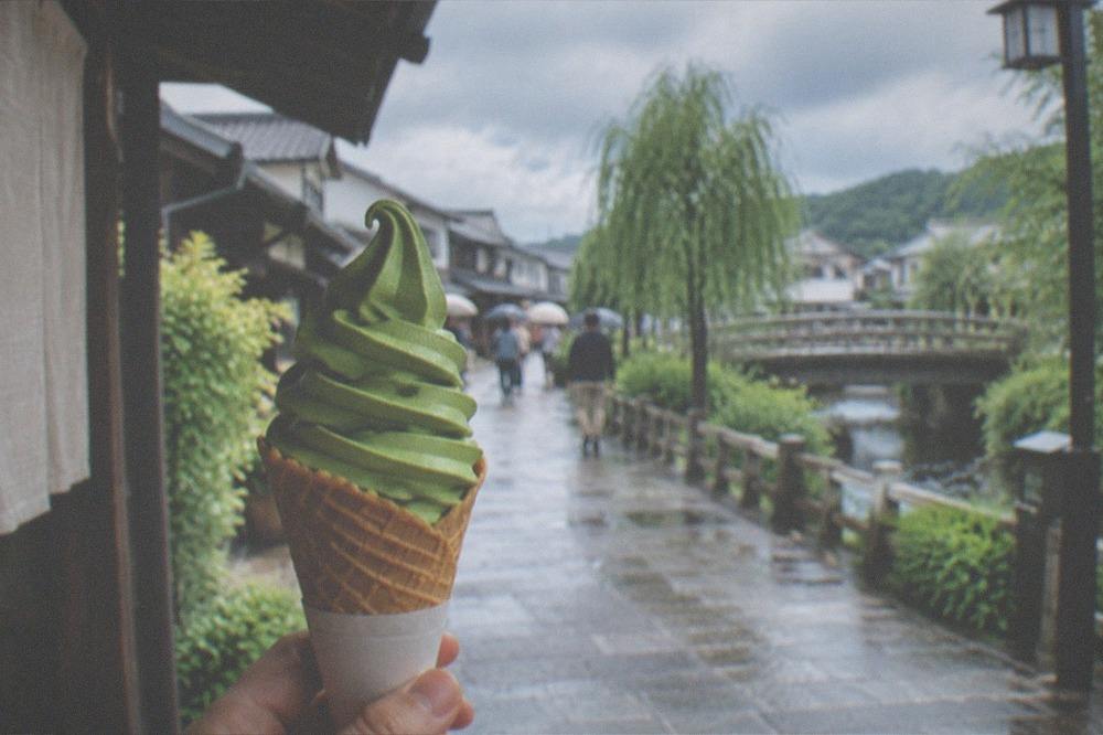 Matcha soft serve ice cream in a cone held up against a traditional street