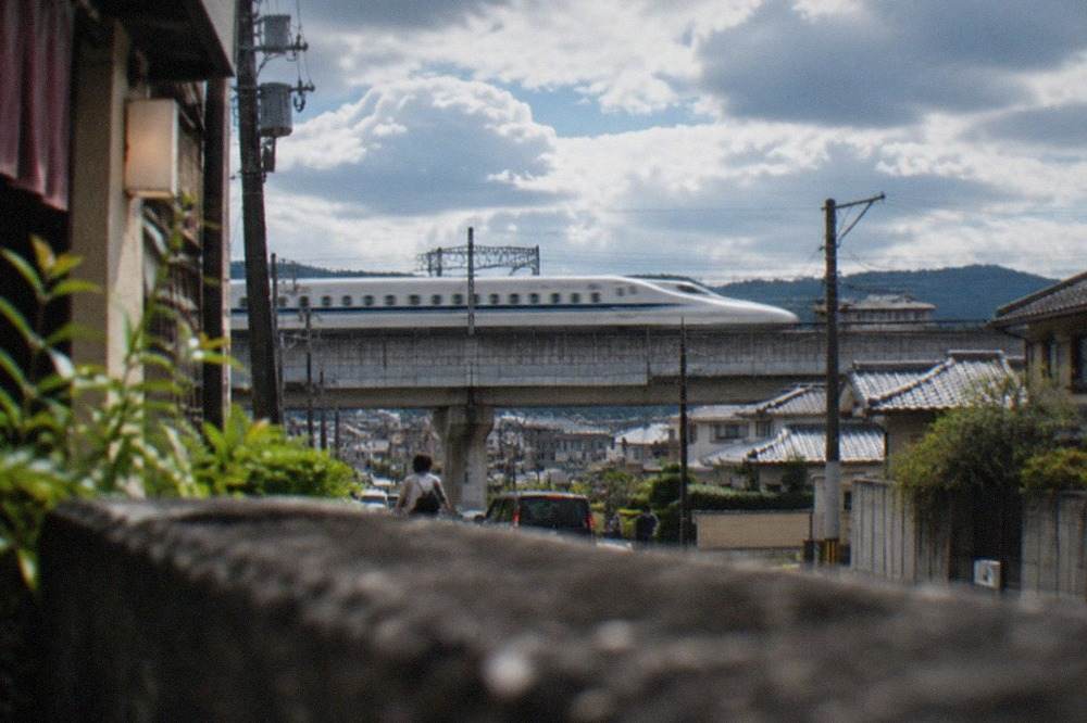 A white bullet train speeding past residential rooftops on an elevated rail line