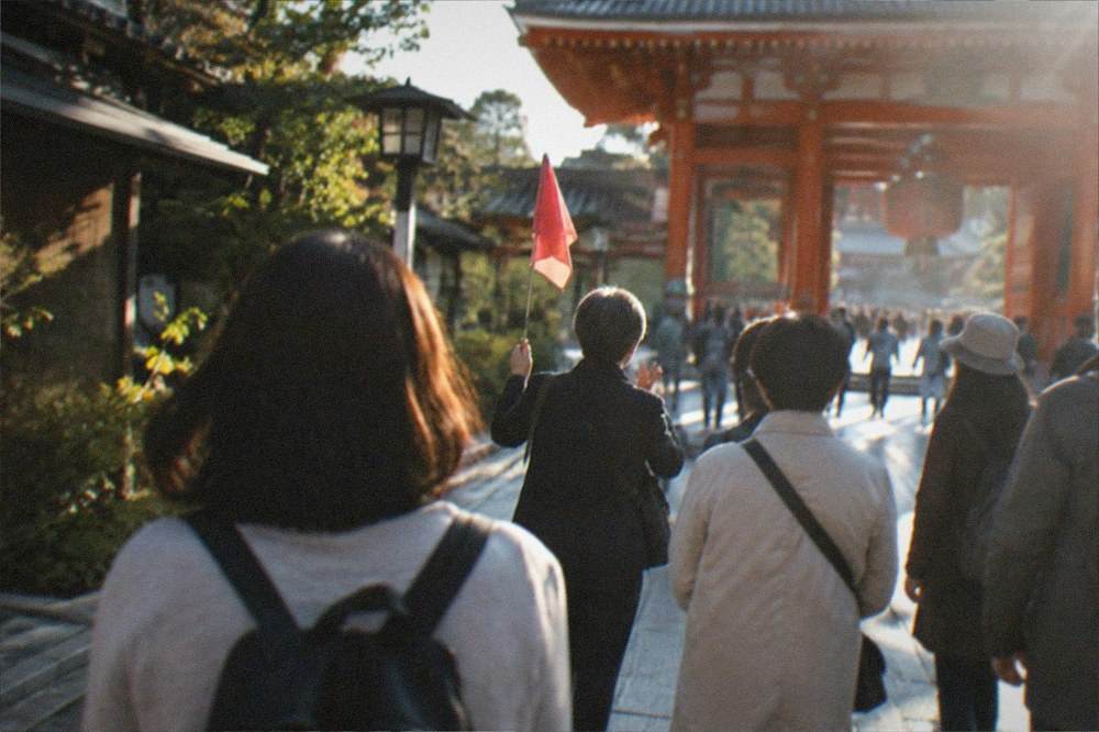 A guide holding a small flag speaking to a group of tourists outside a temple gate