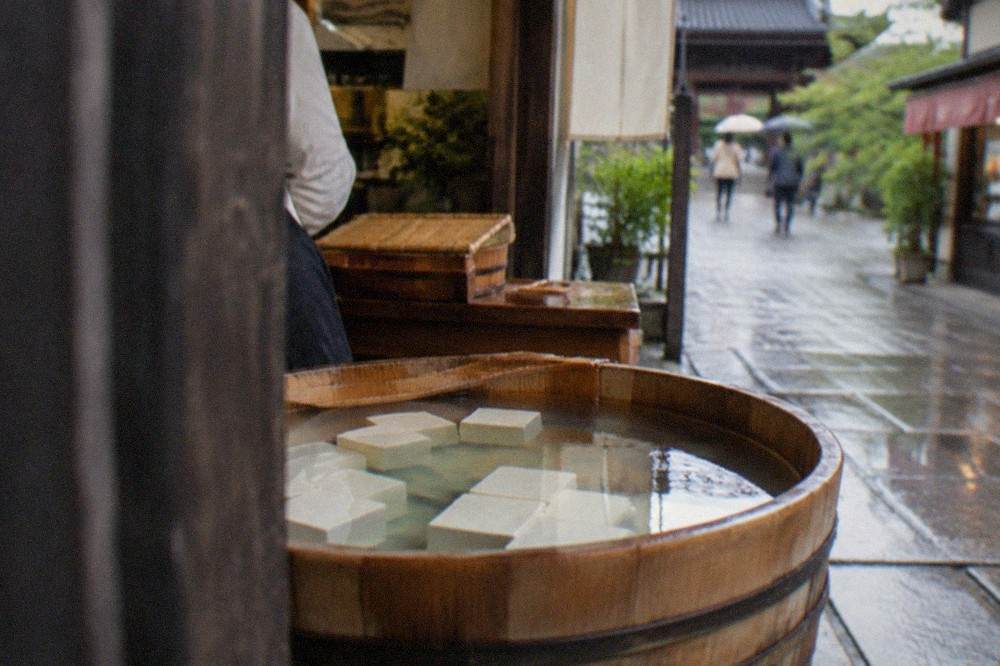 Blocks of fresh tofu resting in cold water in a wooden tub at a traditional Kyoto tofu shop