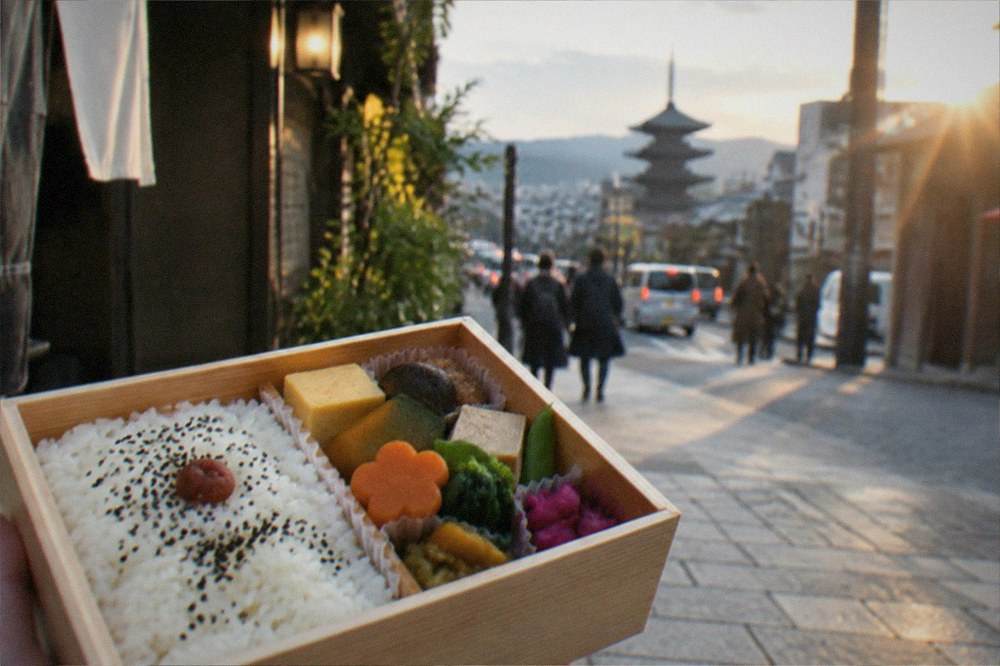 A wooden bento box filled with rice, pickled vegetables, tofu and seasonal vegetable dishes