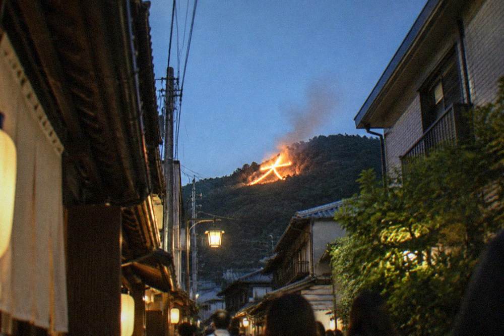 A hillside bonfire character burning above city rooftops at night