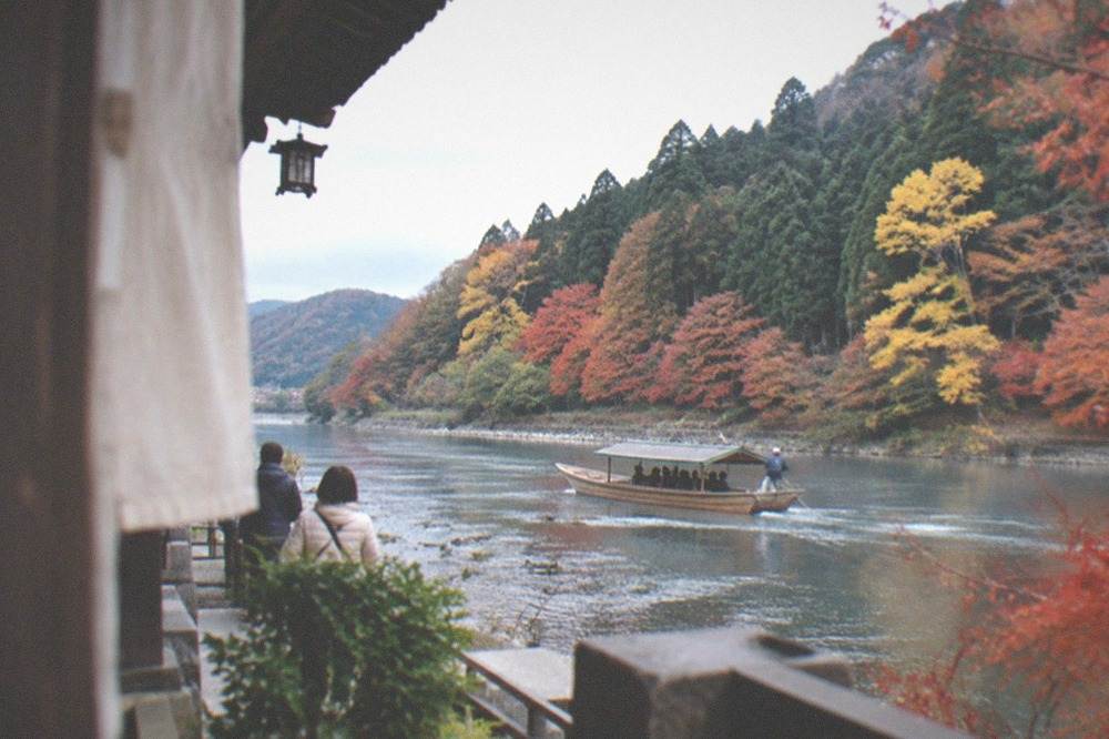 A river boat passing between forested hills with autumn colour