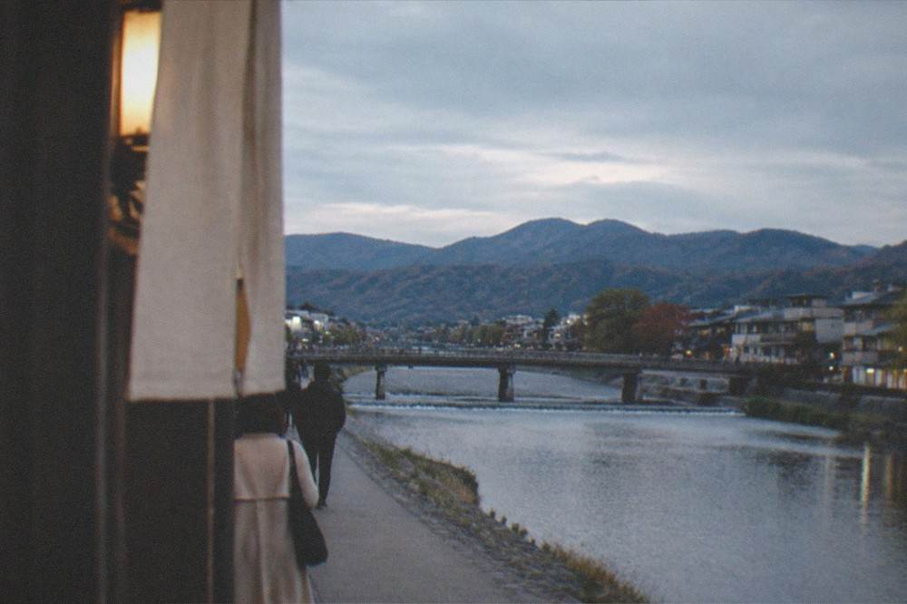 The Kamo River flowing past downtown Kyoto at dusk with the Higashiyama hills behind