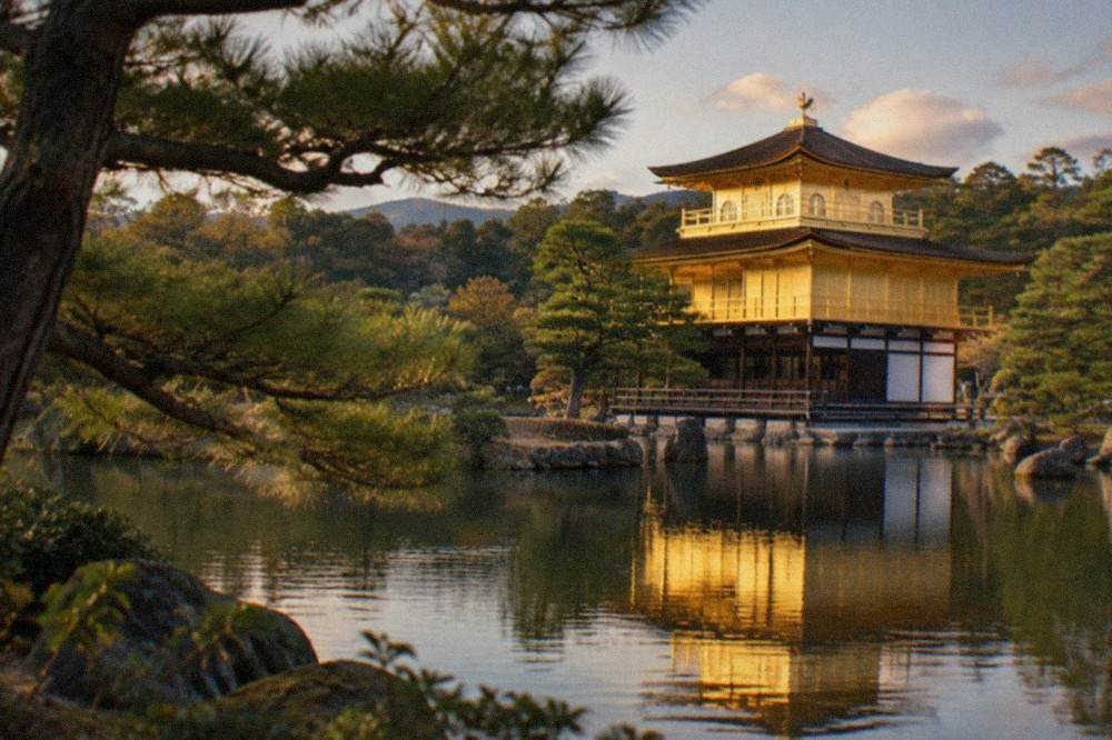The golden pavilion of Kinkaku-ji reflected in the pond beside pine trees