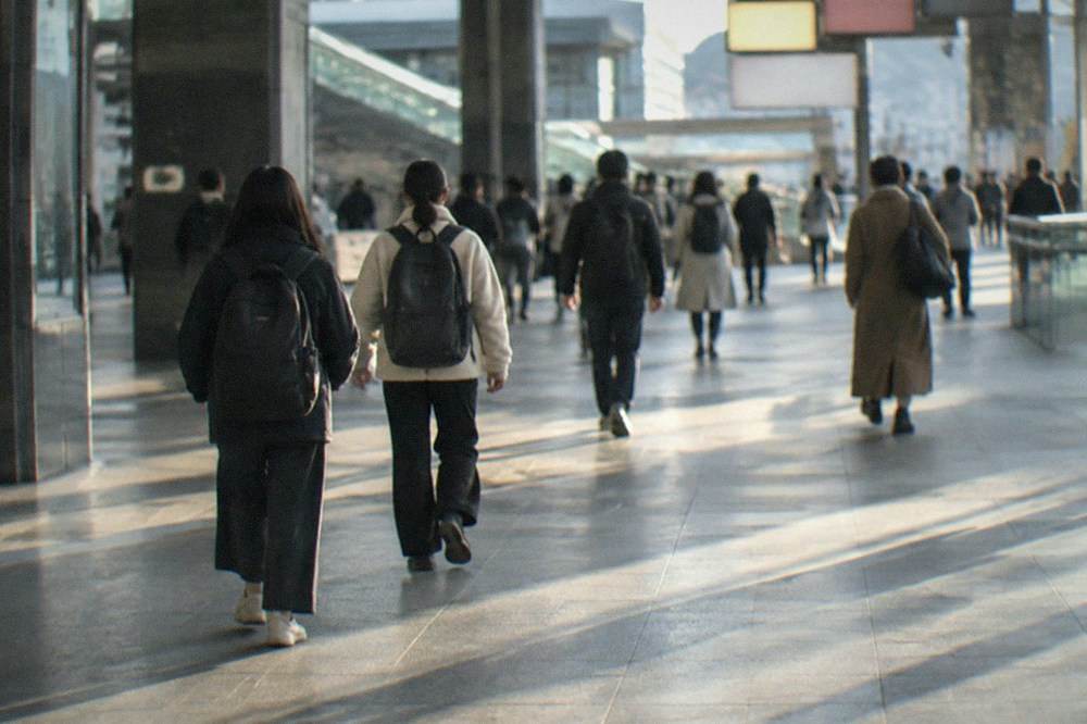Travelers with backpacks walking through a wide concourse of a Japanese rail station past departure boards