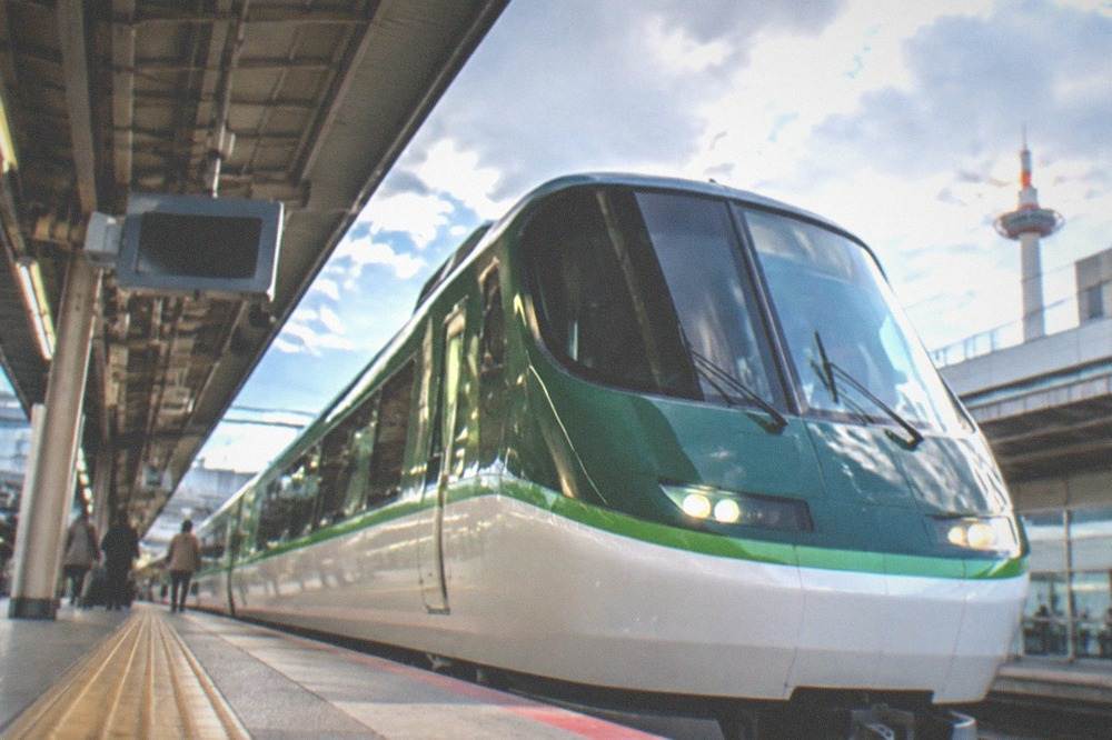 A green and white express train pulling into an airport railway station platform in Japan