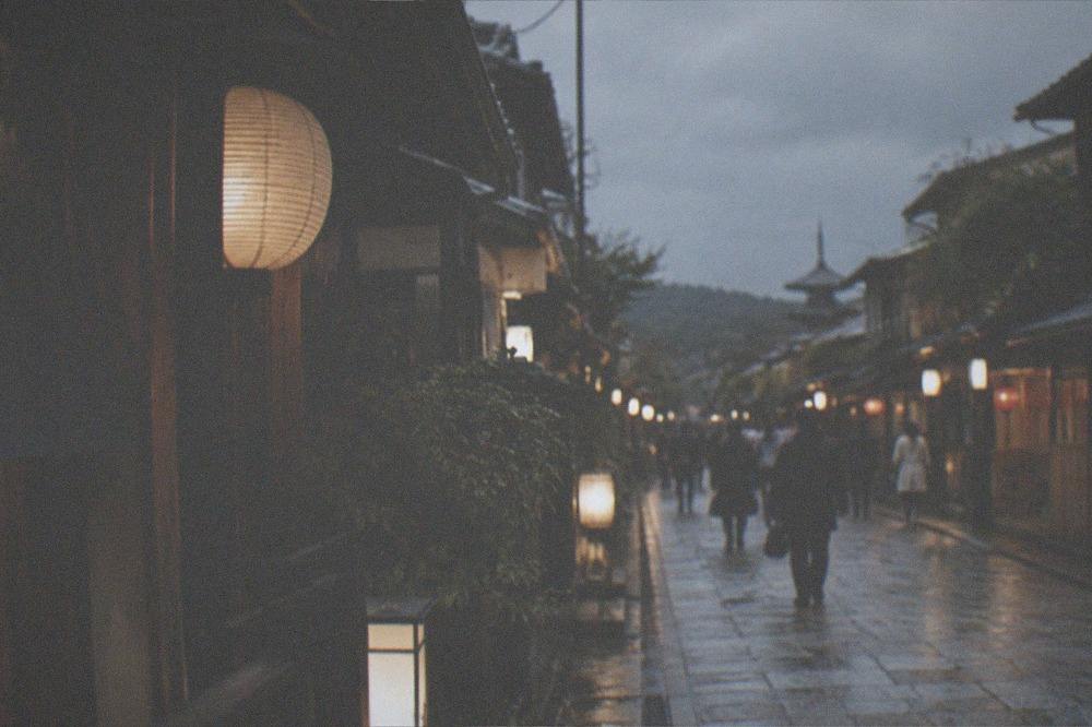 A lantern-lit narrow street in Kyoto's Gion district at night with traditional wooden facades