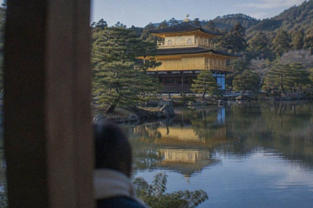 The golden pavilion of Kinkaku-ji reflected in the pond above it, with pine trees on the far bank