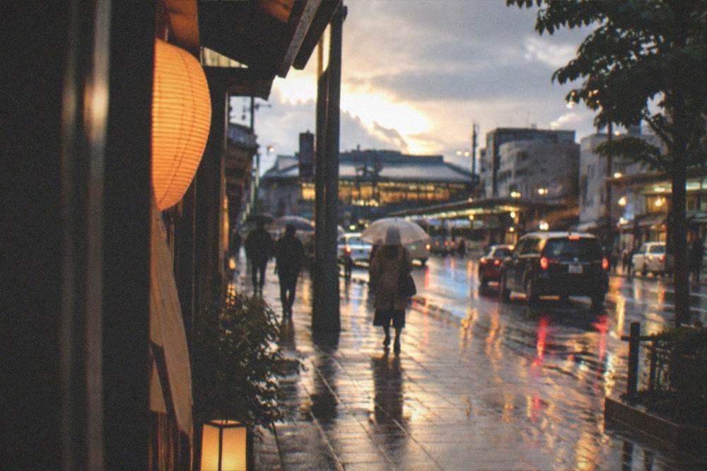 Kyoto street at dusk with wet reflections and warm shop light after rain