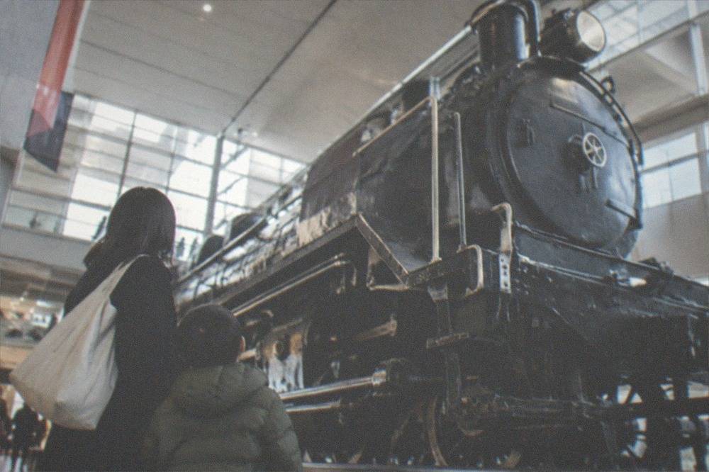 A parent and child looking up at a parked steam locomotive in a bright museum hall