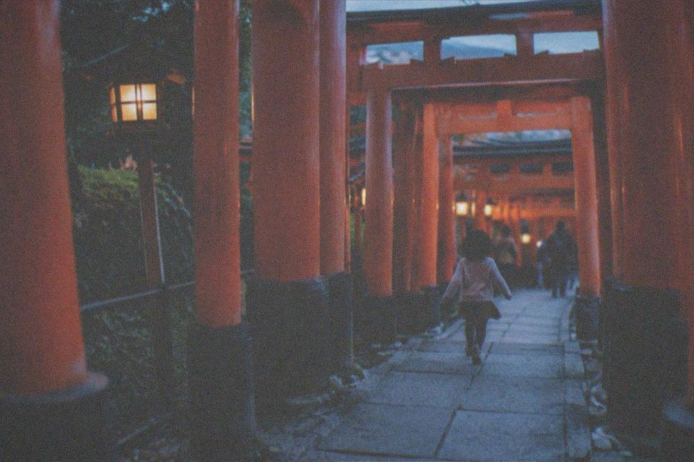 A child running ahead through a tunnel of dense orange torii gates on a mountain path