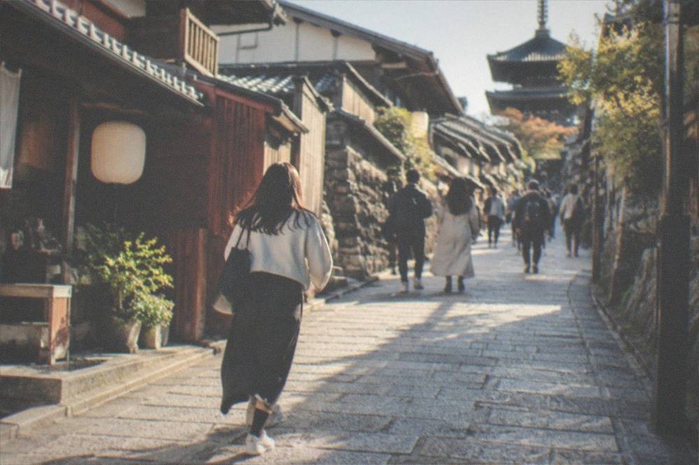 Visitors walking up the stone-paved slope of Ninenzaka toward Kiyomizu-dera in late morning