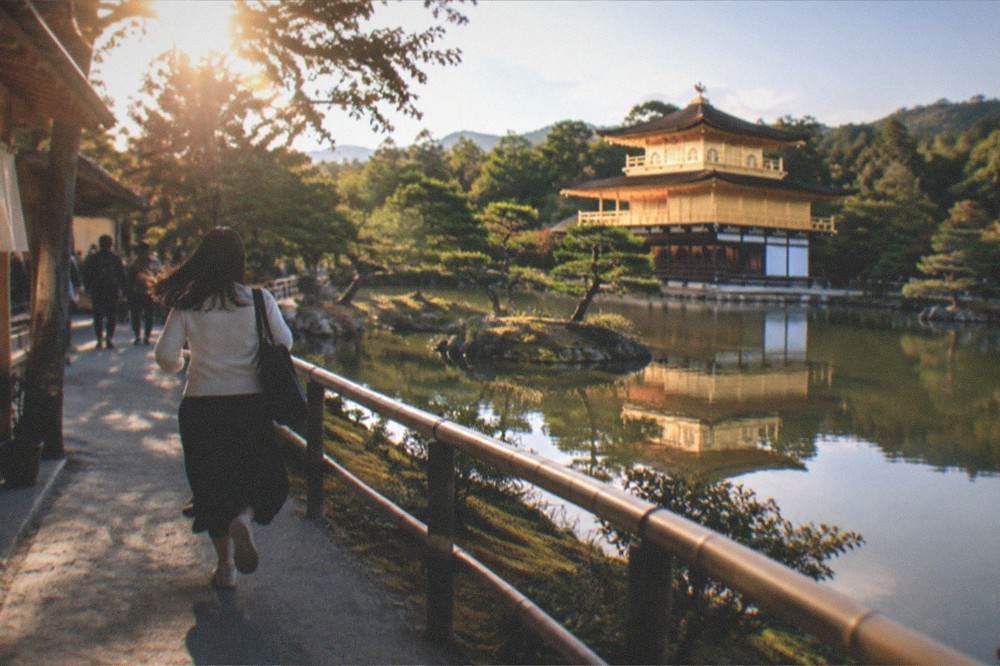 The golden pavilion of Kinkaku-ji reflected in the pond in front of it, surrounded by trees