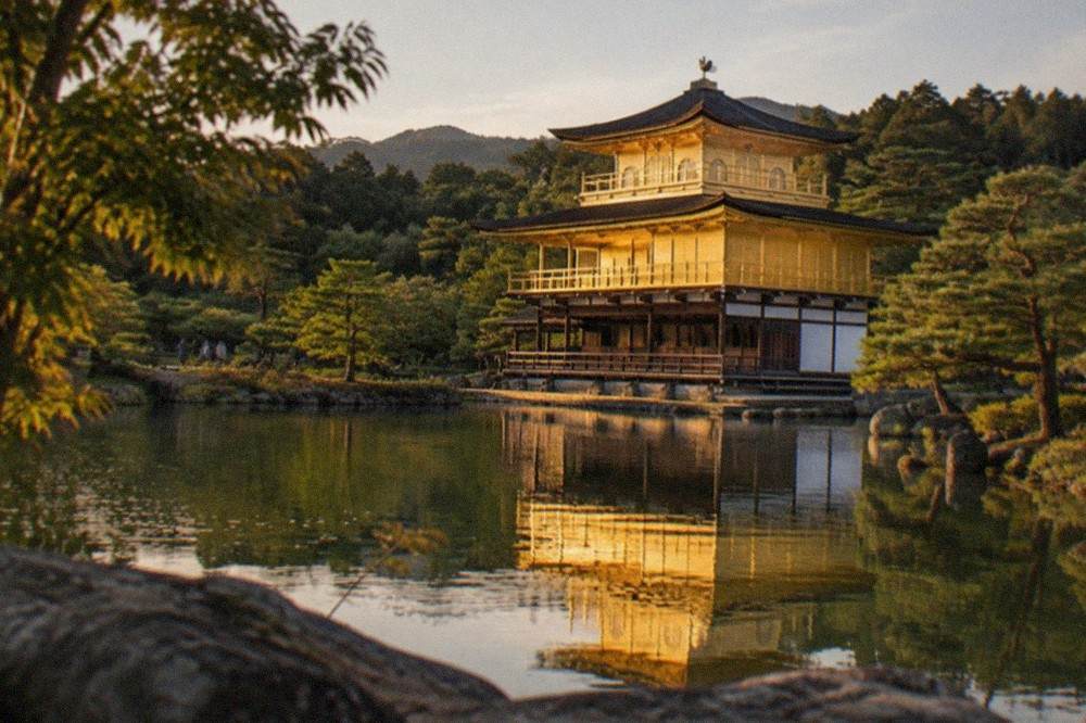 The golden pavilion of Kinkaku-ji reflected in the pond in front of it on a clear afternoon