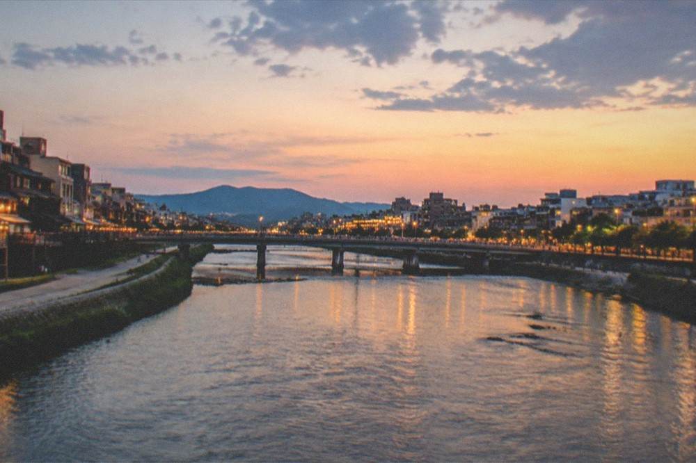 The Kamo river flowing under a bridge at dusk with the city lit along both banks